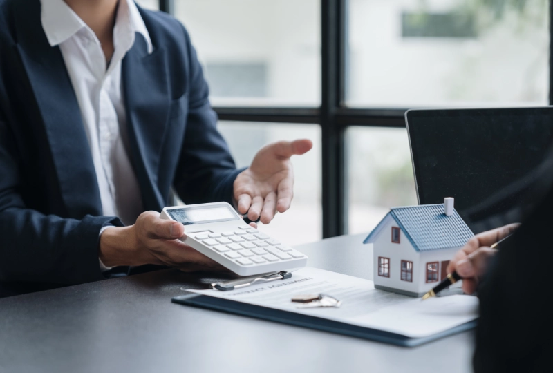 A person is holding a calculator and pointing to the house.